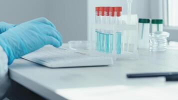 uma dedicada cientista dentro uma Estado da arte laboratório examina vacina amostras dentro teste tubos enquanto digitando em uma especializado teclado, destacando moderno médico pesquisas avançado técnicas video