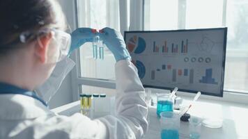A dedicated scientist in a lab coat is conducting complex experiments with biological samples by a bright window, meticulously analyzing results displayed on a nearby computer screen video