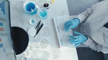 A dedicated scientist in a lab coat and gloves types on a computer, surrounded by lab equipment like petri dishes and solutions, analyzing complex data on a monitor for research and experiments video