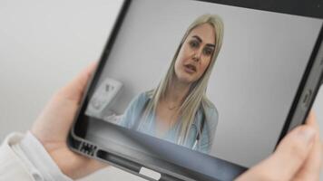 A person is sitting with a tablet in a medical environment, actively participating in a virtual consultation with a professional female doctor who is attentive and focused on their needs video
