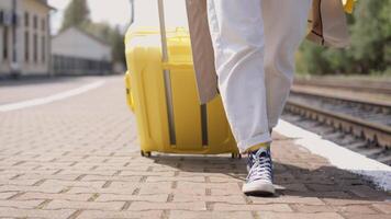 A young woman strolls along a busy railway platform, her shiny yellow suitcase rolling behind her. She is ready for an exciting summer vacation filled with adventure and unforgettable experiences video