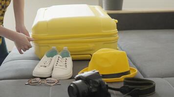 A seasoned traveler organizes their bright yellow suitcase, arranging stylish shoes, a fashionable hat, and a highquality camera, while preparing for an exciting journey full of new experiences video