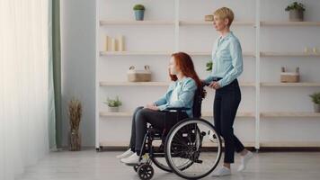 A caregiver gently pushes a girl in a wheelchair towards a bright window. The room has minimalist decor, creating a warm and inviting atmosphere filled with natural light. video