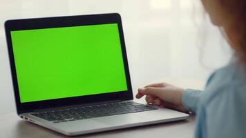 A person sits at a desk, engaged with a laptop that shows a bright green screen. Natural light filters through, illuminating the workspace and creating a calm atmosphere. video