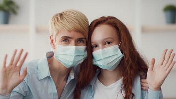 In a cheerful indoor environment, two individuals, an adult and a teenager, smile while wearing face masks and wave their hands in a friendly manner, creating a sense of connection. video