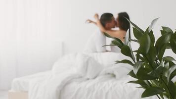 A young couple is embracing and kissing softly in their cozy bedroom. The setting features soft white bedding and natural light, reflecting their love and connection. video