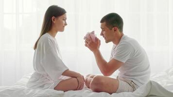 A man and woman sit on their bed in a softly lit bedroom, enjoying each other's company. The couple expresses their love and affection as they connect intimately, creating a warm atmosphere. video