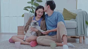 Couple enjoying at home A young couple sits comfortably on the floor of their modern living room, smiling a dog rests between them, creating a cheerful atmosphere video