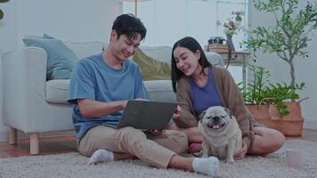 Couple enjoying at home A young couple sits comfortably on the floor of their modern living room, smiling a dog rests between them creating a cheerful atmosphere. video
