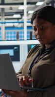 Vertical Happy solar panels facility engineer using laptop to improve efficiency. Smiling African american woman working in photovoltaics factory research and development department, using notebook, camera A video