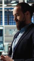 Vertical Portrait of man in solar panels plant using laptop to improve solar cells efficiency. Photovoltaics factory research and development expert using notebook, working on green energy solutions, camera A video