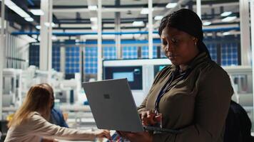 Happy solar panels facility engineer using laptop to improve efficiency. Smiling African american woman working in photovoltaics factory research and development department, using notebook, camera A video