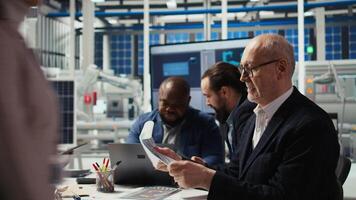 Factory corporate sustainability department team compiling reports on solar panel plant emissions and energy efficiency metrics for regulatory compliance using laptop, camera A video