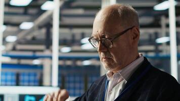 Smiling senior engineer in solar panels plant reading documentation to improve efficiency. Elderly man checking paperwork files in photovoltaics factory research and development department, camera B video