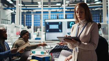 Portrait of smiling scientist in factory using tablet to check PV materials parameters, improving solar panels. Happy researcher develops efficient sustainable energy solutions using device, camera A video