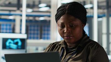 Portrait of smiling engineer in factory uses laptop to check parameters, improving solar panel durability. Happy African american researcher developing efficient sustainable energy solutions, camera B video