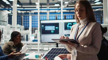 Happy researcher analyzes solar cell prototypes using tablet to optimize energy production. Cheerful solar panels plant expert develops innovative manufacturing tech using device, camera A video