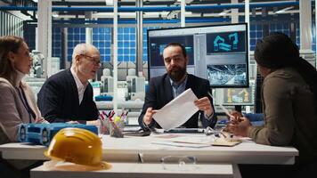 Business executives meet with investors to discuss the integration of automation technology in solar panel production processes, looking over paperwork and schematics, camera A video