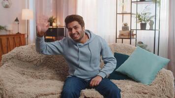 Cheerful Indian young man smiling and waving hello while making conference call at home video