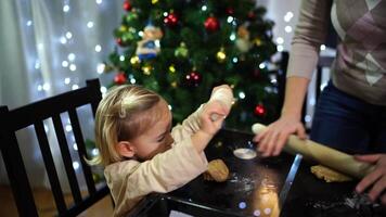 Little girl with her mother roll out the dough for gingerbread cookies with rolling pins on the table video