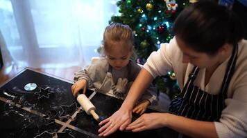 Little girl cuts out cookies from the dough with die-cuts next to her mother at the table video