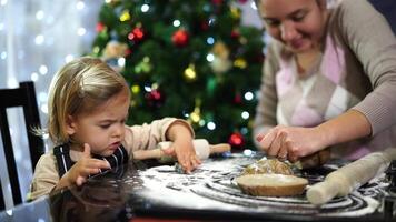 Little daughter runs a cookie cutter across the table while her mother cuts the dough video
