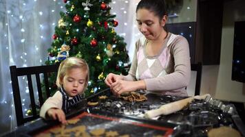 Mom and little girl are stacking cookies cut out of dough on a baking sheet video