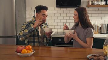 Multicultural couple having breakfast together at the kitchen table. They eat cereal with milk, smile, talk and enjoy a warm and bright morning atmosphere. video