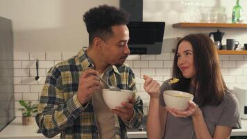Multicultural Couple Enjoying Breakfast Together in Cozy Kitchen. Interracial Young Lovers Eating Cereal, Talking, Laughing and Hugging in the Morning. video