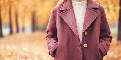 Girl in dark cherry coat with golden buttons stands in a vibrant autumn park, embracing a warm day photo