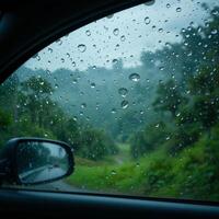 Raindrops scatter over a car window, blurring a lush green landscape seen through the glass. The scene captures a peaceful moment of nature during a rainy drive. photo