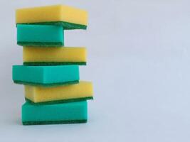 A vertical stack of green and yellow sponges against a plain backdrop, emphasizing cleaning tools suitable for various household tasks. photo