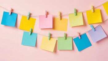 Various colored sticky notes clipped onto a line, displayed against a pink background. The arrangement creates a vibrant and organized visual element suitable for reminders. photo