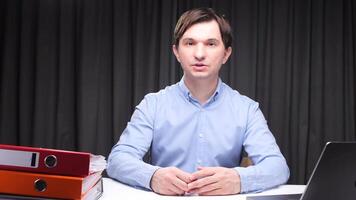 Office worker talking and gesturing at desk with folders and laptop video
