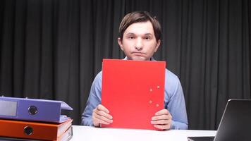 Office worker hiding behind red folder at desk with laptop and binders video