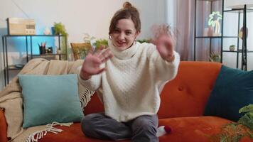 Pretty woman smiling friendly at camera, waving hands gesturing hello, hi, greeting at home on sofa video