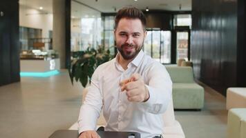 Portrait of Caucasian young businessman pointing to camera choosing hire sitting in office lobby video