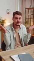 Angry young man raising hands in indignant expression asking reason of failure sitting at table video