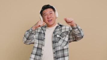 Happy Asian man listening music on headphones and dancing disco fooling around having fun video