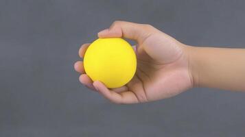Close up of a Hand Holding a Small Yellow Sphere Against a Gray Background photo