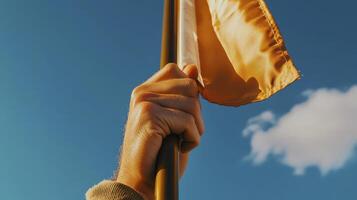 Close Up Hand Holding Golden Flag Against Blue Sky photo