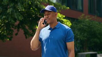 Talking mobile phone calling client ask address communicate with customer purchase receive African American courier guy delivery man postman deliver male in city order food holding paper bag business video