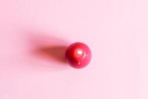 Bright burning paraffin candle in the shape of colorful egg on pink background. photo