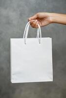 Elegant hand presenting a white shopping bag and gift box isolated on a smooth grey backdrop photo