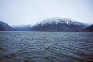Snow-Capped Mountains and Rippling Water Under Overcast Sky photo