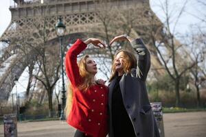 Two female friends form a heart shape with their hands in front of the Eiffel Tower, symbolizing love and friendship in Paris. photo