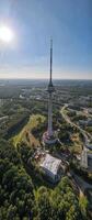 Tall telecommunications tower surrounded by greenery and urban landscape. Aerial view of a modern observation tower with a red and white antenna photo