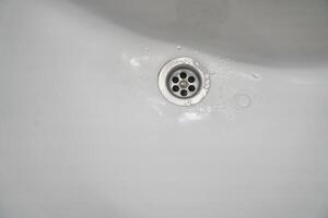 View of a metal drain in a white ceramic bathroom sink. With space to copy photo