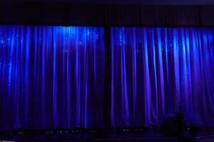 A stage with closed curtains, waiting for the artists to perform. Blue lamps are shining on the stage. With space to copy photo