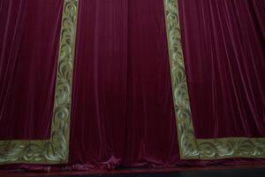 A red curtain with vertical pleats, illuminated in a theatrical setting, showcasing the rich dense texture of the fabric with room to copy photo
